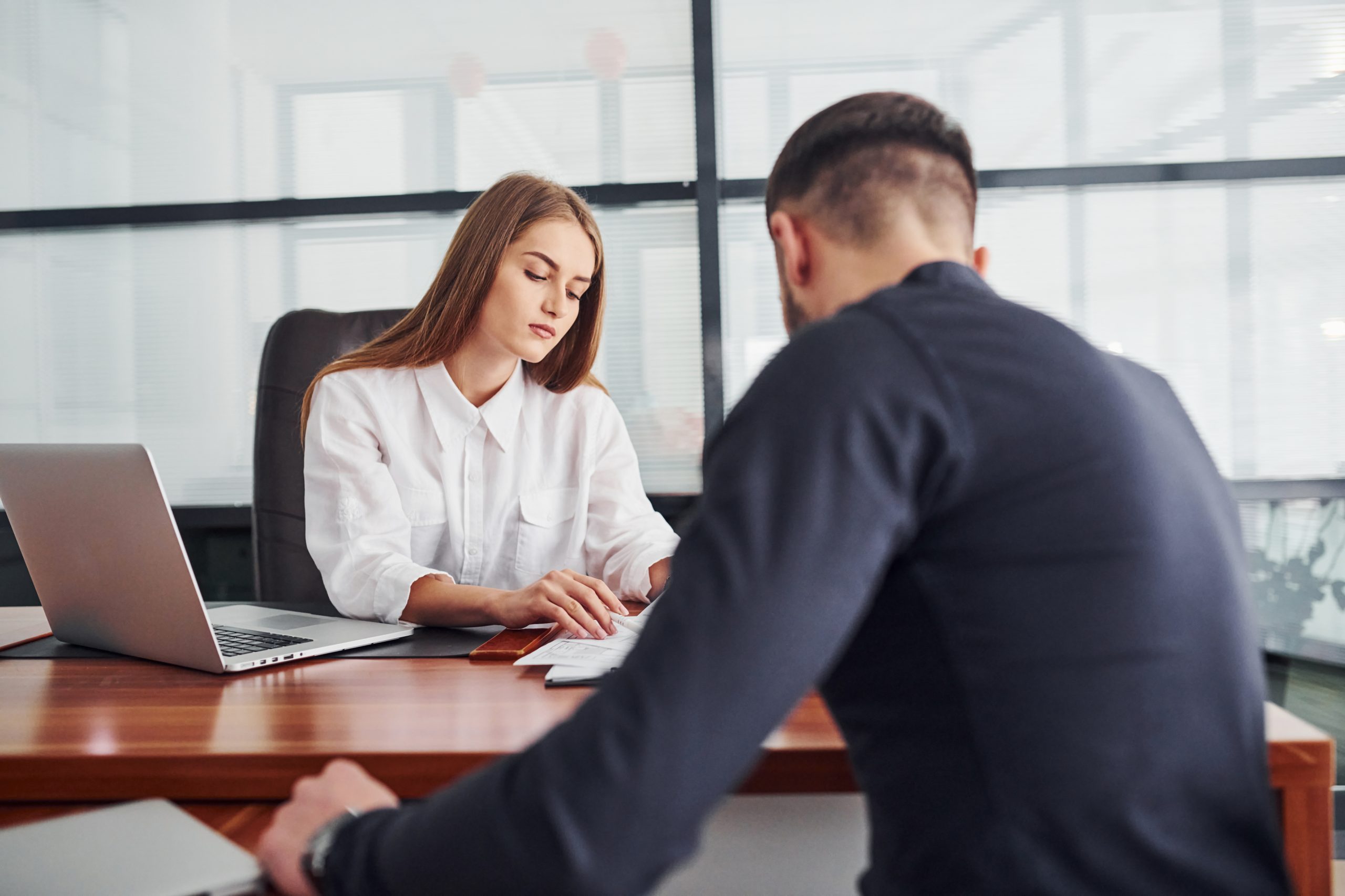 Guy sitting with documents. Woman and man in formal clothes working together indoors in the office by table